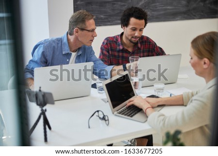 Two men and woman sitting at the table and using laptops stock photo. Teamwork and modern technology concept