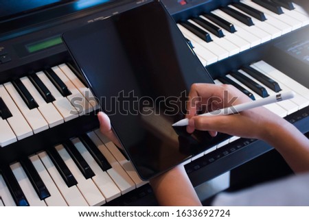 Woman hand holding stylus pencil and writing on black blank screen tablet computer pc with piano background in music room. 