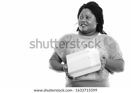 Studio shot of happy fat black African woman smiling and thinking while holding gift box