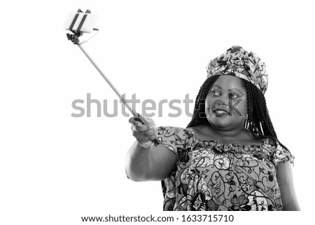 Happy overweight African woman with traditional clothes taking selfie with phone on selfie stick