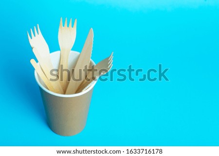 Wooden forks, knives and spoons for food in a paper cup on a colored background. Eco-friendly disposable tableware without plastic.