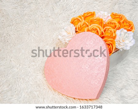 Orange roses and white flowers in a pink box in the shape of a heart on a white background from fur.  A gentle romantic gift for your beloved on Valentine's Day.