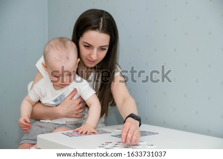Mom and baby are sitting at the table and playing a board game. The kid is studying the pictures on the cards.