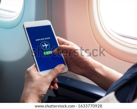 Flight mode concept. Hand holding white smartphone and turned on airplane mode on screen near the window on the airplane. Royalty-Free Stock Photo #1633770928