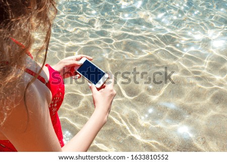 Young girl in a red swimsuit is taking a photo of the sea with her mobile phone on her vacation. Beach concept.