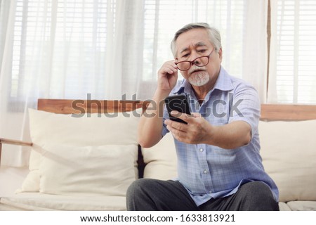 Older men move glasses down to look at the phone in the hand due to Hyperopia problems, which makes vision difficult.Health problems of the elderly. Royalty-Free Stock Photo #1633813921
