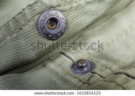 Two collapsible parts of the unbuttoned metal snap button fastener, mounted on the outerwear olive color close-up at shallow depth of field Royalty-Free Stock Photo #1633816123