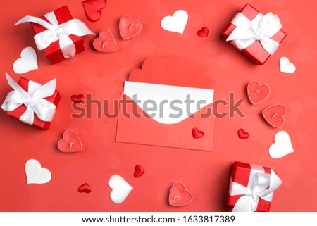 Mail envelope with a blank greeting card surrounded by gifts and hearts on a red background. Love, Valentine Day or Wedding greeting concept.