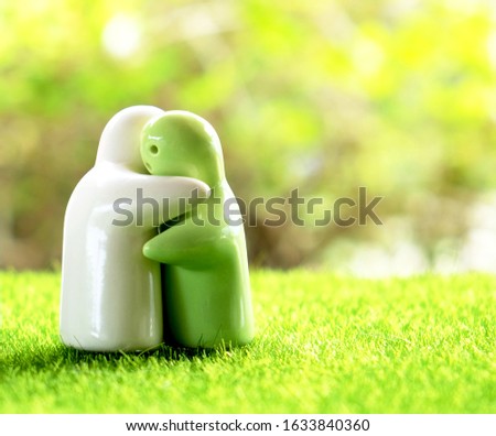 White and green ceramic hugging couple figurine on green grass and bokeh nature background. Concept for anniversary, love, romance, wedding, or Valentine’s day