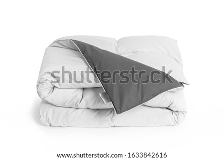 Folded soft white duvet, blanket or bedspread with the gray back side and empty white label, against white background. Close up photo Royalty-Free Stock Photo #1633842616