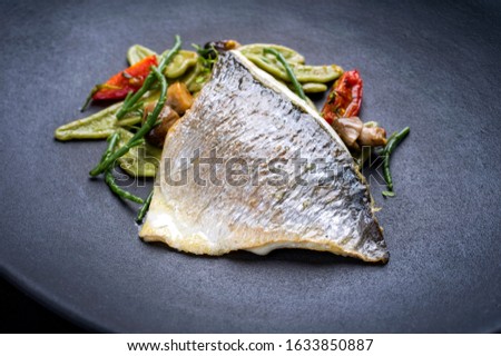 Gourmet fried Italian gilthead fish filet with spinach pasta, glasswort and tomatoes as closeup on a modern design plate 