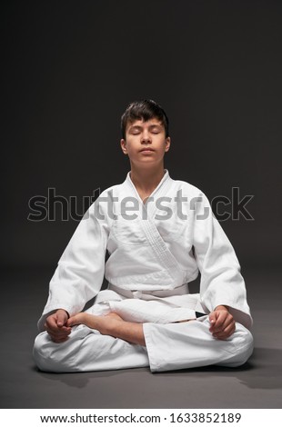 a teenager dressed in martial arts clothing meditating on a dark gray background, a sports concept