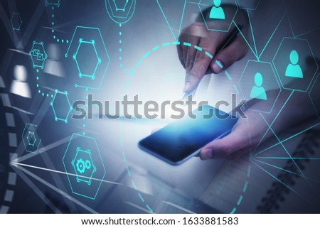 Hand of businessman with smartphone at blurry office table with double exposure of HUD social network interface. Concept of recruitment and social media. Toned image