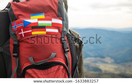 travel life style passion concept picture of backpack with country flags stripes of Ukraine, Germany, Austria, Denmark, Norway, Hungary and Czech Republic blurred background mountains highland view 