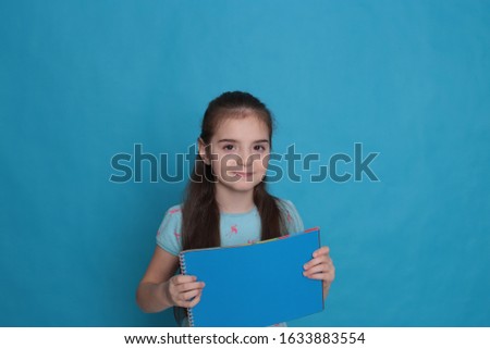 Cheerful loving girl of eight years old and a colored sheet of paper free space for recording on a azure background