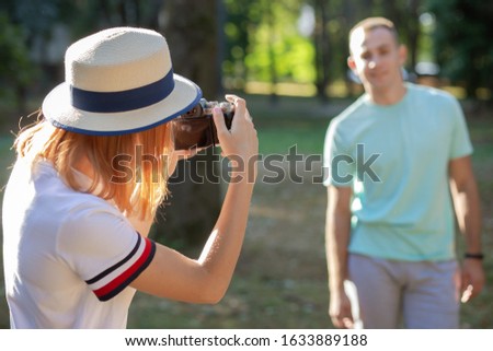 Young teenage couple taking pictures of one another outdoors in sunny summer park.