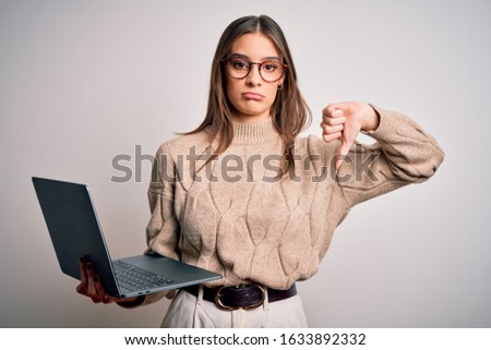 Young beautiful brunette woman working using laptop over isolated white background with angry face, negative sign showing dislike with thumbs down, rejection concept