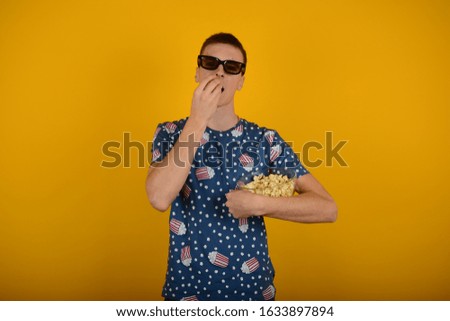 man in 3D glasses eats popcorn in a colored T-shirt on a yellow background