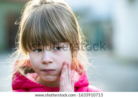 Portrait of a pretty child girl holding her hand to cheek in pain outdoors.