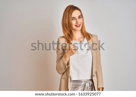 Redhead caucasian business woman standing over isolated background doing happy thumbs up gesture with hand. Approving expression looking at the camera showing success.
