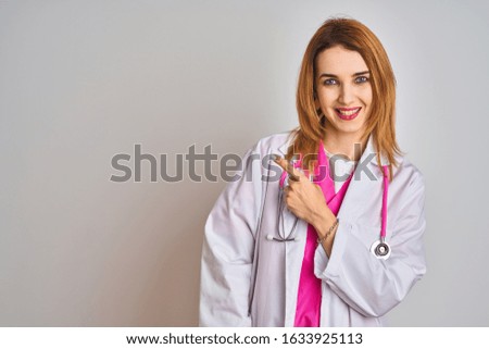 Redhead caucasian doctor woman wearing pink stethoscope over isolated background cheerful with a smile of face pointing with hand and finger up to the side with happy and natural expression on face