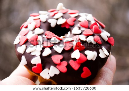 Chocolate donut with bright heart-shaped confectionery. Photo for culinary sites, blogs, desserts, restaurants, cafes. Dessert for a loved one. The 14th of February. Sweets for a holiday, a gift.