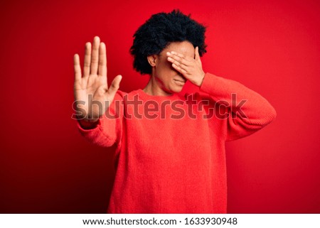 Young beautiful African American afro woman with curly hair wearing casual sweater covering eyes with hands and doing stop gesture with sad and fear expression. Embarrassed and negative concept.