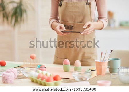 Cropped portrait of unrecognizable young woman taking smartphone photo of Easter eggs composition in art studio, copy space