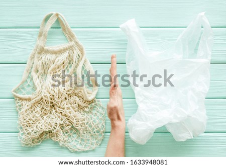 Zero waste concept. Hand between textile and plastic bag on green wooden background top-down