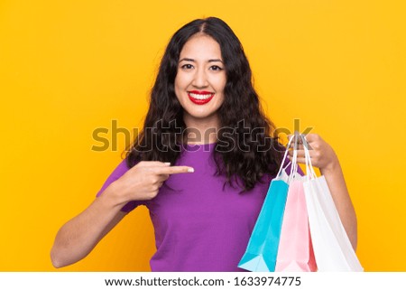 Spanish Chinese woman with shopping bag over isolated background and pointing it