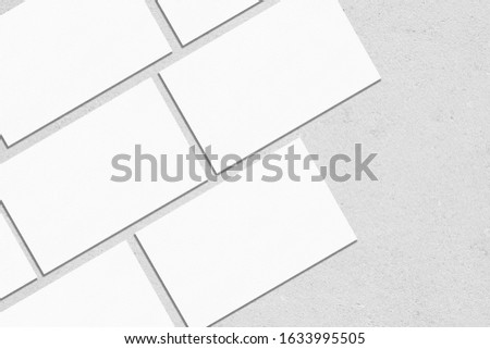 Closeup of empty white rectangle business card mockups lying diagonally on neutral grey concrete background. Flat lay, top view. Open composition. Blank Template for Corporate Identity. Copy space