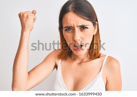 Beautiful redhead woman wearing casual white t-shirt over isolated background annoyed and frustrated shouting with anger, crazy and yelling with raised hand, anger concept