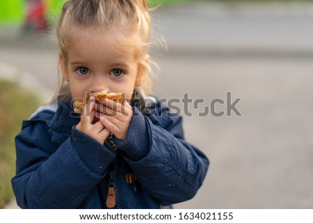 A beautiful little Caucasian girl with blond hair and eating bread eagerly with her hands looks at the camera with sad eyes, an abandoned child and hungry.