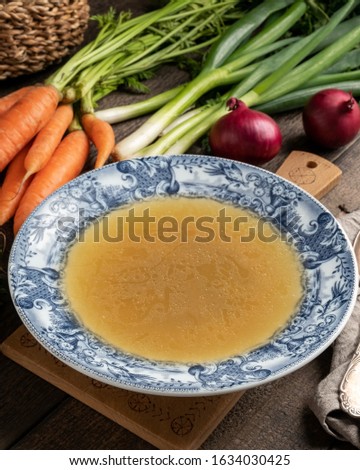 Chicken stock in a vintage plate, with fresh vegetables in the background