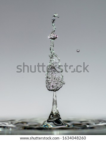 Water drops form mesmerizing transparent sculptures when falling into light blue clear water, drops and splashes close-up.