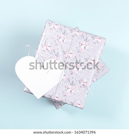Gift boxes wrapped with grey paper with floral pattern and white paper heart  on light blue background. Valentine's day, Women's day or Mother's day mockup. Top view, close up. Square photo.