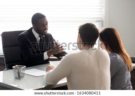 Rear view couple during meeting with African ethnicity family lawyer, spouses and realtor negotiating about rental property, banker worker consulting first realestate purchasing lease mortgage concept Royalty-Free Stock Photo #1634080411