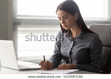 Focused employee sit at workplace hold pen writing noting working with documents do paperwork puts signature on business letter, works on project, female student studying online learns course concept Royalty-Free Stock Photo #1634083186