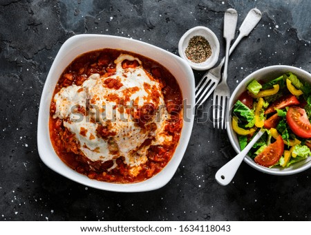 Turkey tomato sauce mozzarella cheese meatloaf and fresh tomato yellow bell pepper vegetables salad on a dark background, top view. Healthy balanced diet food