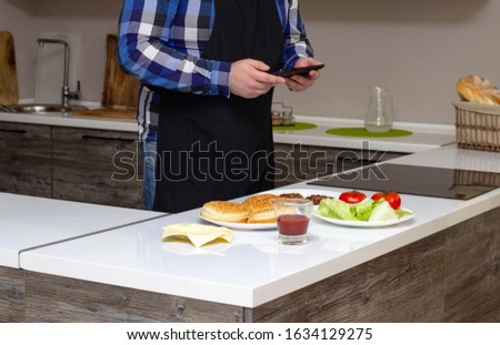 Man photographs cooking home burger on the phone, background