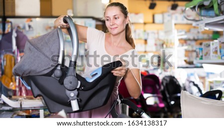 Smiling pregnant woman choosing portable baby carriage in children shop