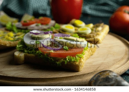 Combination with different kinds of sandwiches on the wooden board: with mushrooms, with avocado and eggs, with ham lettuce and tomatoes, with avocado and seeds. Top views