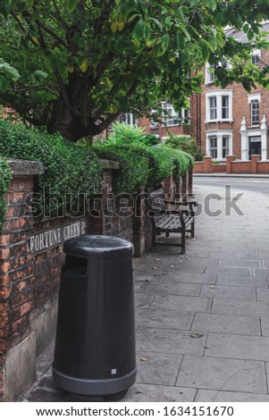 Fortune Road name sign on a brick wall, trash bin and a wooden bench next to the wall, Hampstead, London. A street name sign is a type of traffic sign used to identify named roads