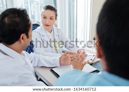 Serious female chief doctor listening to her employees at daily meeting