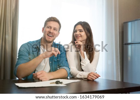 young happy couple man and woman sitting in their new cosy apartment after successful lease sign both smiling.