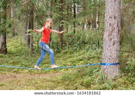 Tween girl balancing on slackline during summer holidays Royalty-Free Stock Photo #1634181862