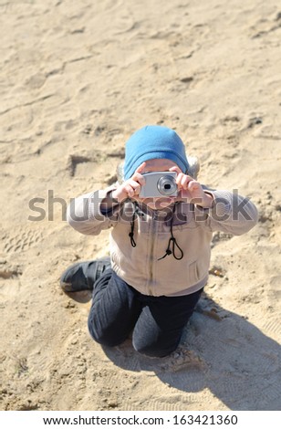 Funny little child holding a compact camera upside down to take pictures outdoors, shot from high angle