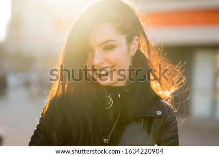Girl in black with black aggressive make up is standing in a city and smiling. Might be a picture representing subculture, youth, teenagers, alternative style etc. 