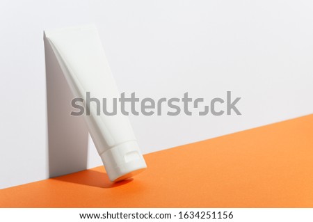 Cream tube on bright sunny orange background. Cosmetic skincare product blank plastic package. White unbranded lotion, balsam, hand creme, toothpaste mockup. Sunscreen cream bottle Royalty-Free Stock Photo #1634251156