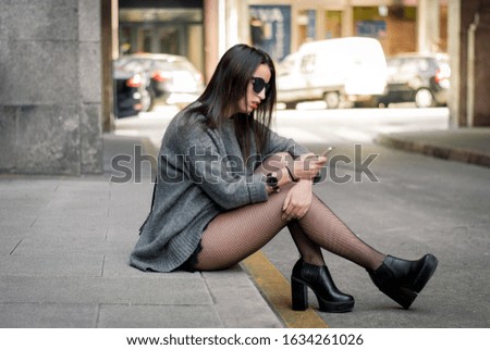 Girl or woman using a smartphone sitting on the sidewalk while waiting for her friends bored